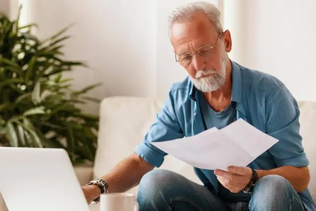Starszy mężczyzna z laptopem i dokumentami zastanawia się, czy krus wlicza się do stażu pracy w budżetówce.