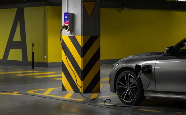 Szary samochód elektryczny ładuje się przy wallboxie. Ranking firm montujących ładowarki do samochodów elektrycznych.