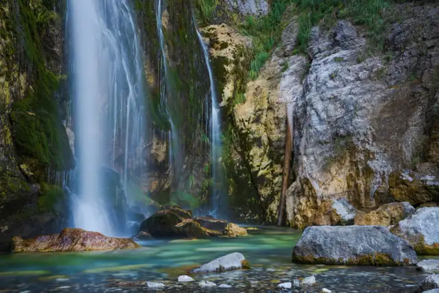 Wodospady w Albanii: kaskady wody spływają po omszałych skałach do turkusowej rzeki.