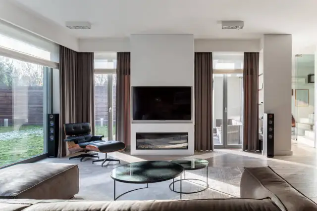 Nowoczesne zasłanianie okien w salonie z kominkiem i wygodnym fotelem.
