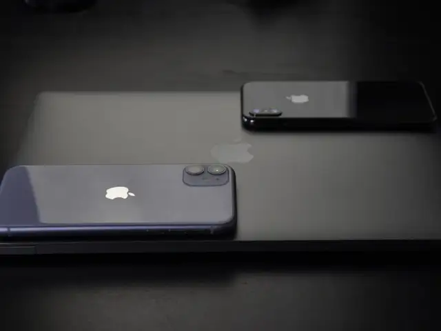 Dwa iPhone'y, w tym jeden fioletowy, leżą na czarnym laptopie. Zastanawiasz się, jak wyłączyć iPhone'a 11?