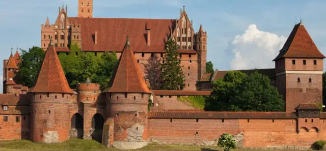Potężny zamek w Malborku, wpisany na listę UNESCO w Polsce, z czerwonymi dachami i zielenią.