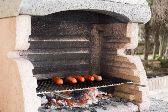Grill z cegieł z pieczonymi kiełbaskami na ruszcie nad żarem.