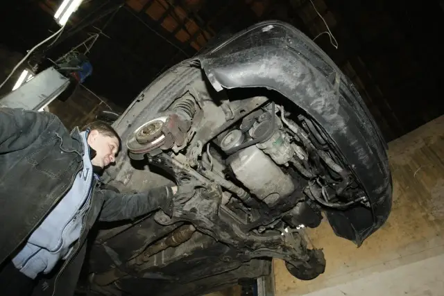 Mechanik ogląda podniesiony samochód, widok od spodu, widoczne podzespoły silnika i zawieszenia.