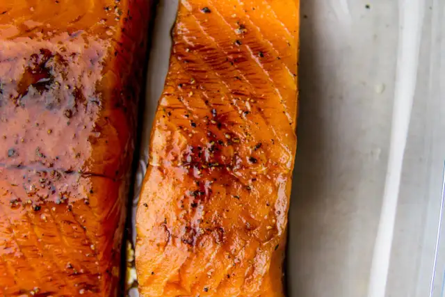 Dwa kawałki soczystego łososia w sosie sojowym, błyszczące i doprawione pieprzem, gotowe do podania.