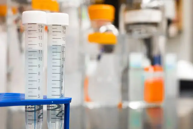 Dwie probówki z płynem w stojaku laboratoryjnym, w tle sprzęt badawczy.