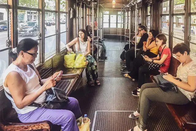 Wnętrze tramwaju w Mediolanie. Pasażerowie korzystają z mediolańskiej komunikacji miejskiej, przeglądając telefony.