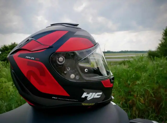 Czerwono-czarny kask motocyklowy HJC RPHA 70 z przyciemnianą blendą, gotowy na podróż pośród zieleni.