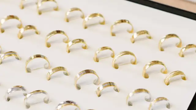 Rzędy złotych i dwukolorowych obrączek na białym tle.