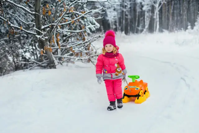 Mała influencerka w zimowym lesie ciągnie zabawkę. Zastanawiasz się, ile zarabiają dzieci influencerów za udział w kampaniach reklamowych?