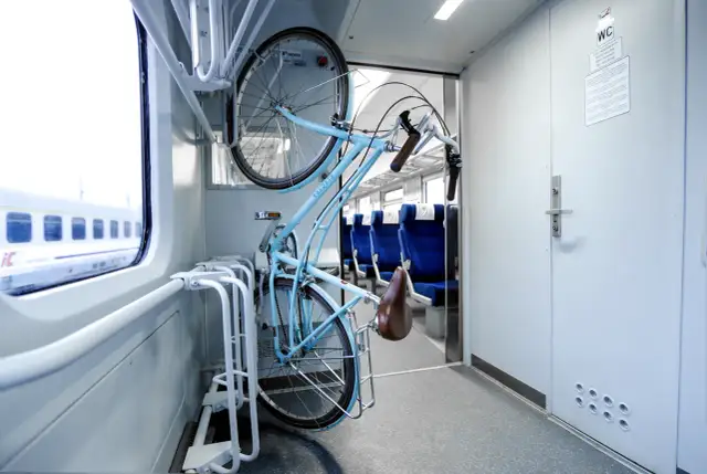 Błękitny rower zawieszony w specjalnym stojaku w wagonie PKP. Planujesz podróż i zastanawiasz się, jak kupić bilet na rower PKP? To proste!