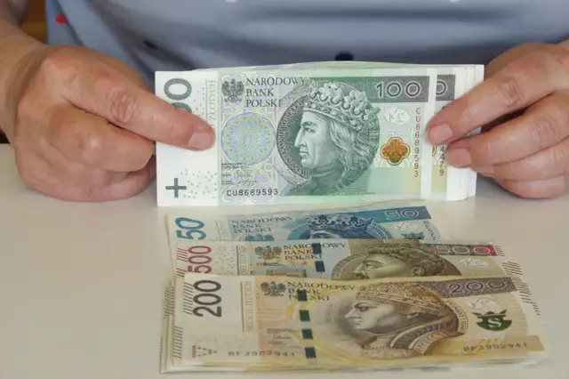Ręce trzymają stos banknotów 100 zł. Pod spodem leżą banknoty 50, 500 i 200 zł. Pytanie: co po zasiłku rehabilitacyjnym?