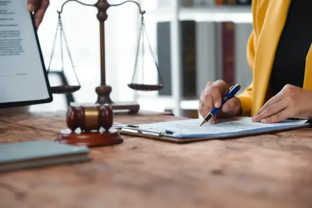 Przygotowanie do egzaminu prawniczego: młoda prawniczka analizuje dokumenty, obok młotek sędziowski i waga sprawiedliwości.