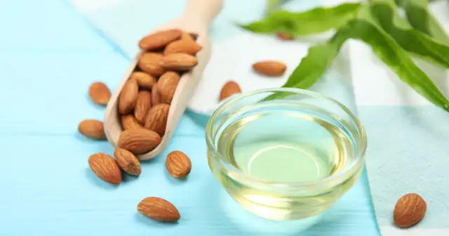 Odkryj cudowne **olej migdałowy właściwości**! Na zdjęciu migdały w drewnianej łyżce i miseczce z czystym olejem.