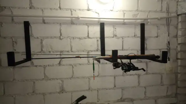 Wieszak na wędki z kołowrotkiem i spławikiem, zamontowany na białej ceglanej ścianie.