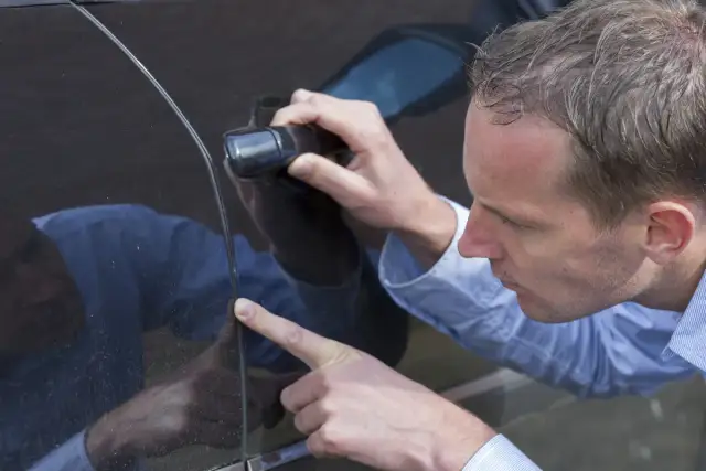 Mężczyzna ogląda czarne drzwi samochodu, wskazując palcem na zabrudzenie.