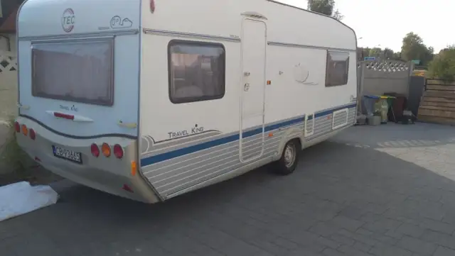 Biała przyczepa kempingowa TEC Travel King z niebieskimi pasami, gotowa na wakacyjne podróże.