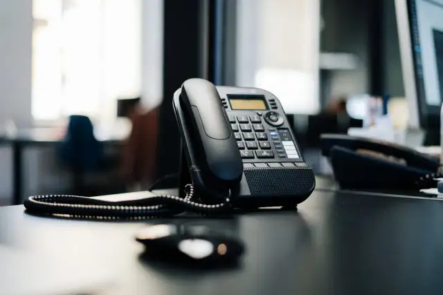 Czarny telefon biurowy na biurku. Słychać dzwonek, jakby numer zablokowany dzwonił, ale nikt nie odbiera.
