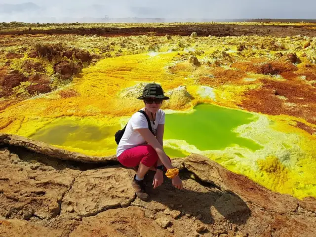 Kobieta w kapeluszu siedzi na skale, podziwiając surrealistyczne, żółto-zielone krajobrazy kotlina danakilska.