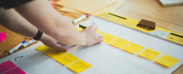 Ręce układają żółte karteczki z notatkami, tworząc mapę myśli. To kluczowy etap planowania strategii firmy.