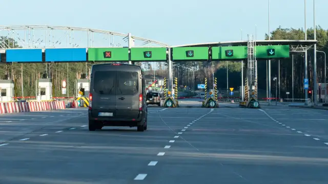 Czarny van zbliża się do bramek autostradowych z zielonymi znakami kierunkowymi.
