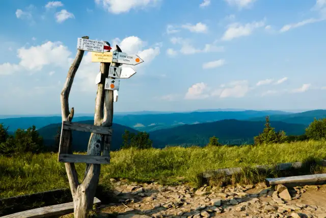 Gdzie w góry na majówkę? Znaki wskazują szlaki, a za nimi rozciągają się zielone wzgórza i błękitne niebo.