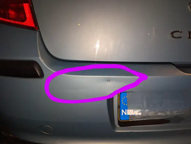 Wgnieciony plastikowy zderzak samochodu z fioletowym obramowaniem.