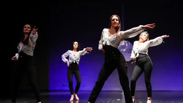 Kobiety w białych koszulach i czarnych spodniach tańczą na scenie. Pokazują, jak tańczyć solo na dyskotece, pewne siebie i pełne gracji.