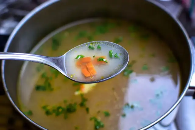 Łyżka z bulionem, marchewką i zieloną pietruszką, idealna do rosołu wegetariańskiego.