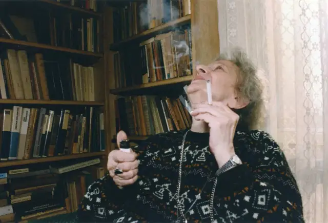 Wisława Szymborska, zapalając papierosa, otoczona książkami. Ciekawe, o czym myślała?