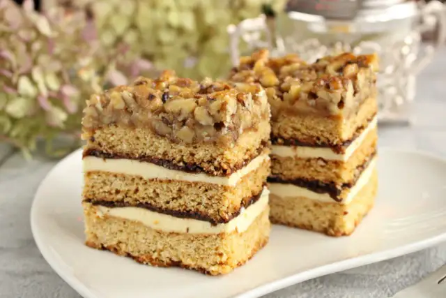 Pyszny miodownik z orzechami, przełożony kremem i czekoladą, prezentuje się apetycznie na białym talerzu.