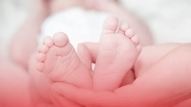 Dłonie trzymające stopy noworodka.