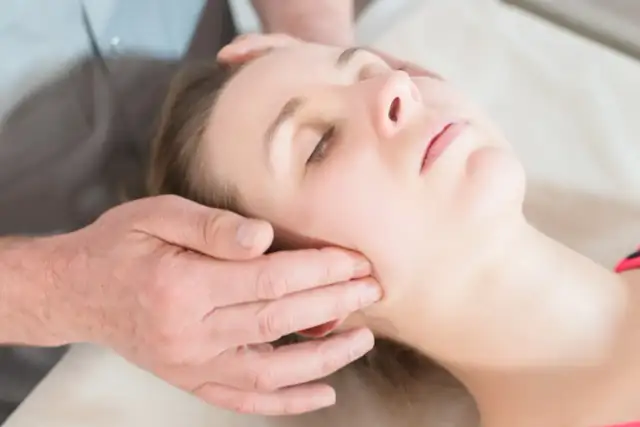 Delikatny masaż twarzy, który pomaga jak rozluźnić szczękę. Dłonie terapeuty obejmują policzek i skroń.