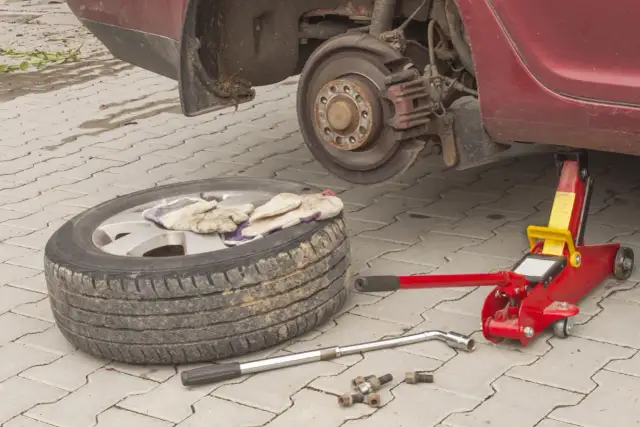 Koło zapasowe, podnośnik, klucz i śruby leżą obok podniesionego samochodu.