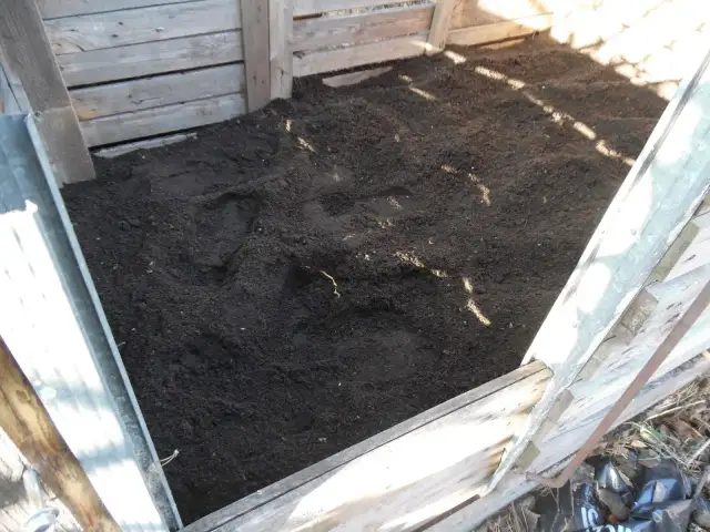 Gotowy kompostownik, w którym trwa kompostowanie na gorąco. Ciemna, żyzna ziemia czeka na wykorzystanie w ogrodzie.