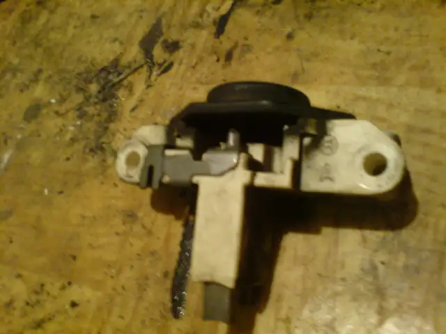 Szczotkotrzymacz alternatora z widocznymi szczotkami na drewnianym tle.