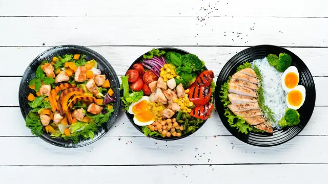 Trzy talerze z lekkostrawnym obiadem dla matki karmiącej: sałatka z dynią i kurczakiem, miska z kurczakiem, warzywami i jajkiem, oraz kurczak z makaronem ryżowym i jajkiem.