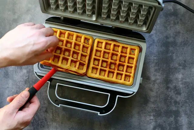 Ręce wyjmują złociste gofry z gofrownicy. Idealne na przepis na gofry bezglutenowe.