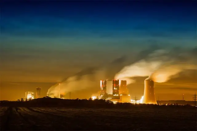 Dymiące kominy elektrowni nocą, ukazujące przyczyny zanieczyszczenia powietrza.