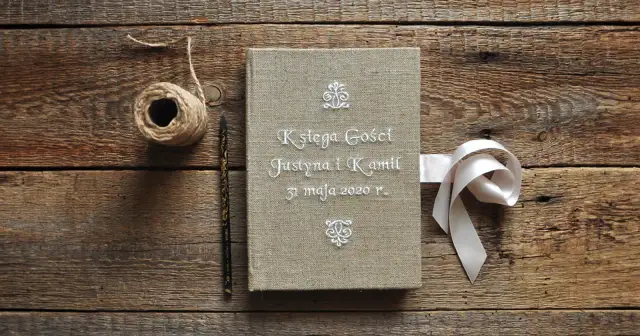 Oto pomysł co zamiast księgi gości na weselu: lniana księga z imionami Justyny i Kamila, ozdobiona wstążką.