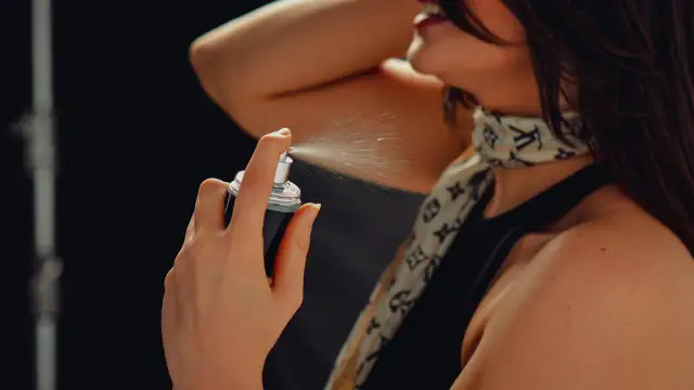 Kobieta rozpyla mgiełkę perfum na szyję.