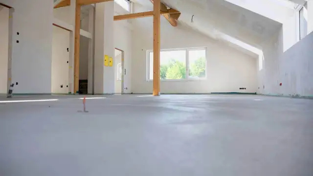 Nowe wnętrze z drewnianymi belkami i oknem. Podłoga gotowa pod wykończenie, zastanawiasz się, ile za metr wylewki?