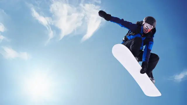 Snowboardzista w powietrzu, biała deska snowboard jak dobrać. Słońce i chmury na niebieskim tle.