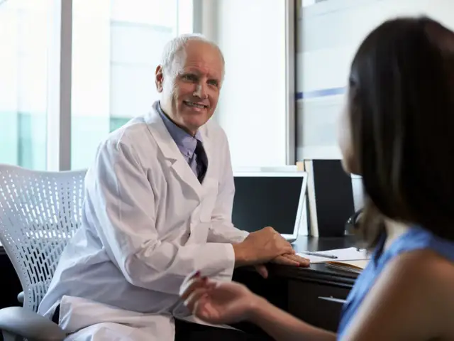 Lekarz w białym kitlu rozmawia z pacjentką przy biurku.