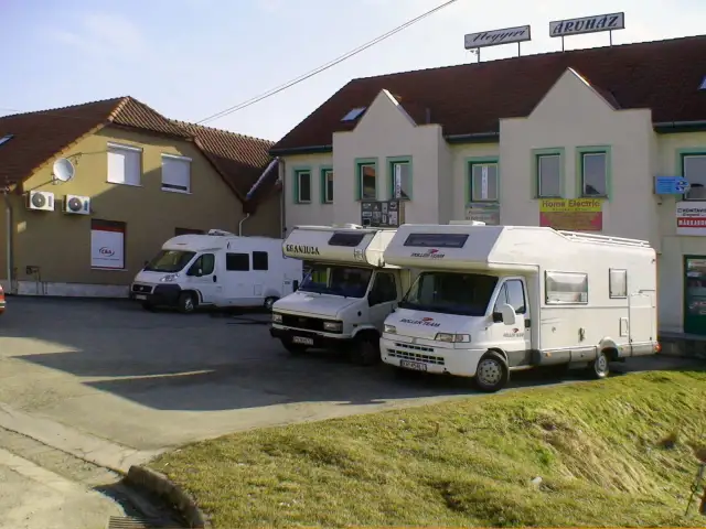 Trzy białe kampery zaparkowane przed budynkami z szyldami.