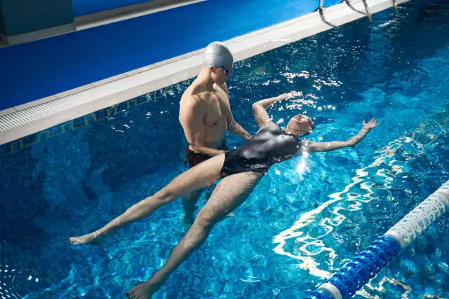 Instruktor pomaga kobiecie w nauce pływania. Zastanawiasz się, ile kosztuje godzina nauki pływania?