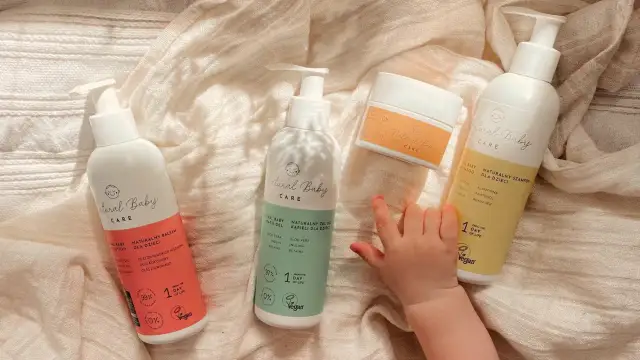 Naturalne kosmetyki dla noworodka: balsam, żel do kąpieli i szampon. Dziecięca rączka sięga po nie.