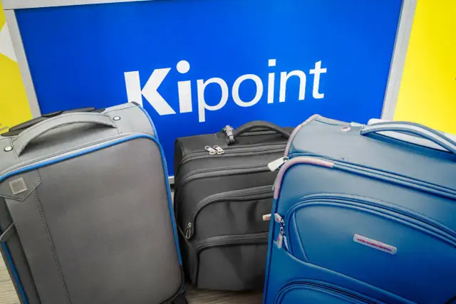 Three suitcases in front of a blue sign with "Kipoint" in white letters.