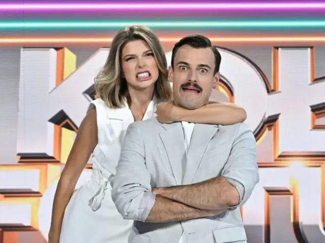 Para z minami na tle studia "Koło Fortuny Tak czy Nie". Ona go dusi, on ma przerażoną minę.