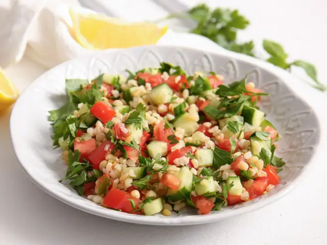 Orzeźwiająca sałatka z kaszą bulgur, pomidorami, ogórkiem i natką pietruszki, podana na białym talerzu.